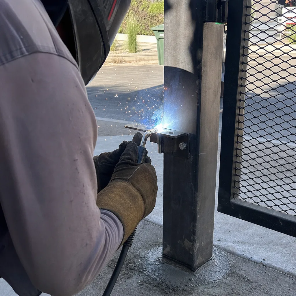 Welder installing a steel hinge bracket on a metal gate post